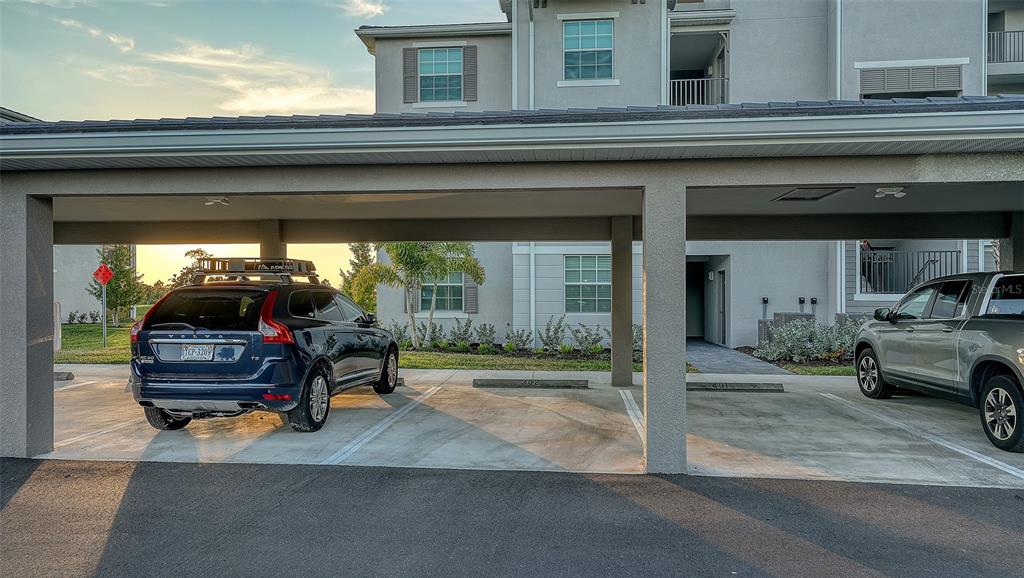 A covered parking area with two vehicles parked in front of a multi-story apartment building — 17655 OPAL SAND DRIVE UNIT 302, VENICE, FL