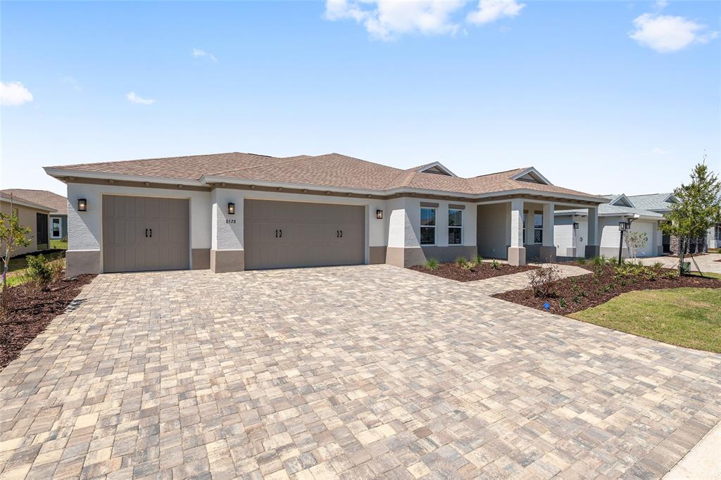 A single-story house with a three-car garage and a paved driveway under a blue sky — 8528 SW 101ST AVENUE, OCALA, FL