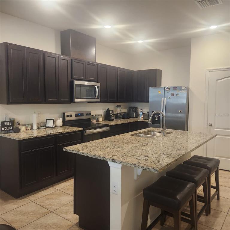 A kitchen features dark wood cabinets, granite countertops, a center island, and stainless steel appliances — 1636 THICKET AVENUE, DAVENPORT, FL