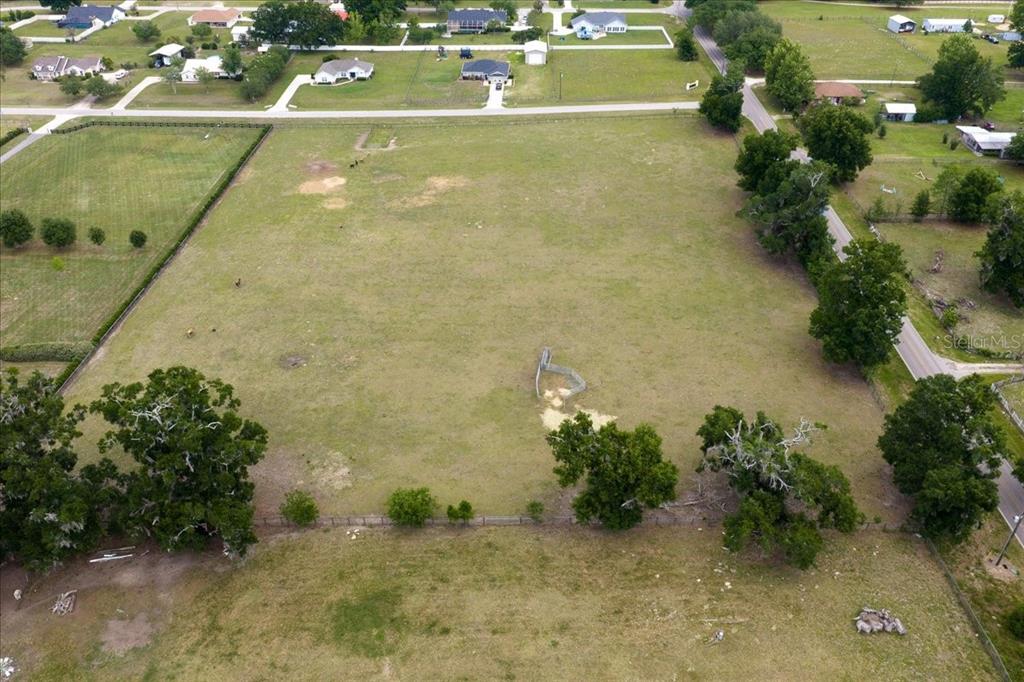 An aerial view shows a large, grassy, fenced-in lot with scattered trees and nearby houses — TBD NE 106TH STREET, ANTHONY, FL