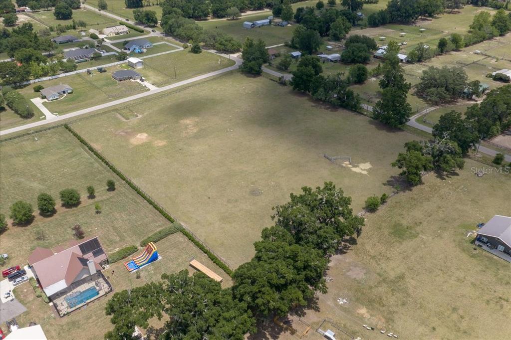 An aerial view shows a large, open grassy field bordered by trees and residential properties — TBD NE 106TH STREET, ANTHONY, FL
