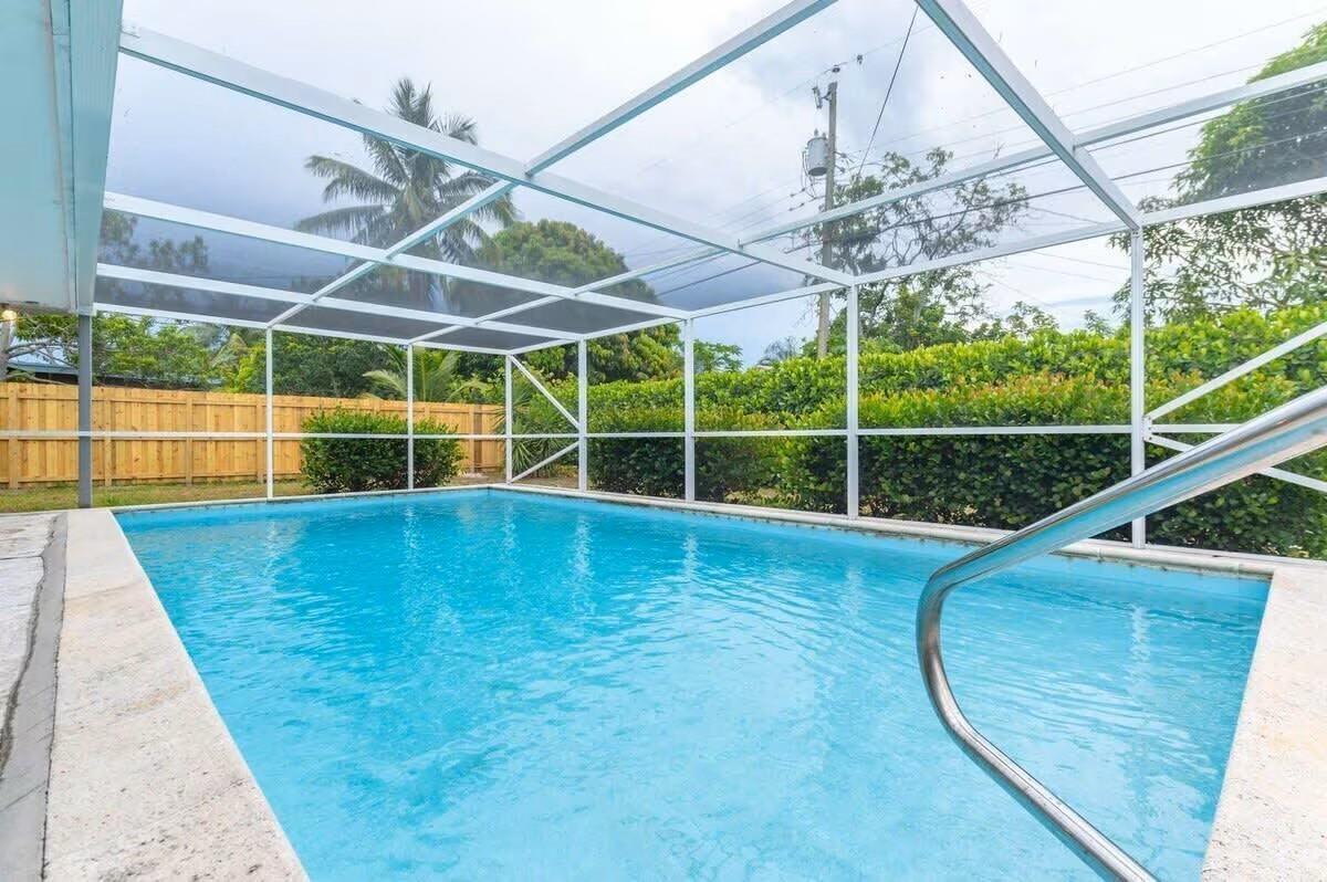 A swimming pool enclosed by a white screen cage sits in a backyard with landscaping — 176 SE 27th Place, Boynton Beach FL 33435, BOYNTON BEACH, FL