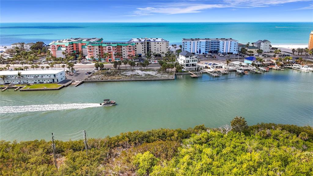 An aerial view shows a waterway with a boat, surrounding buildings, and coastal vegetation — 18450 GULF BOULEVARD UNIT 401, INDIAN SHORES, FL