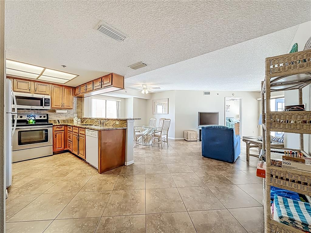 An open-concept kitchen with wood cabinets and tile floors flows into a dining area — 18450 GULF BOULEVARD UNIT 401, INDIAN SHORES, FL
