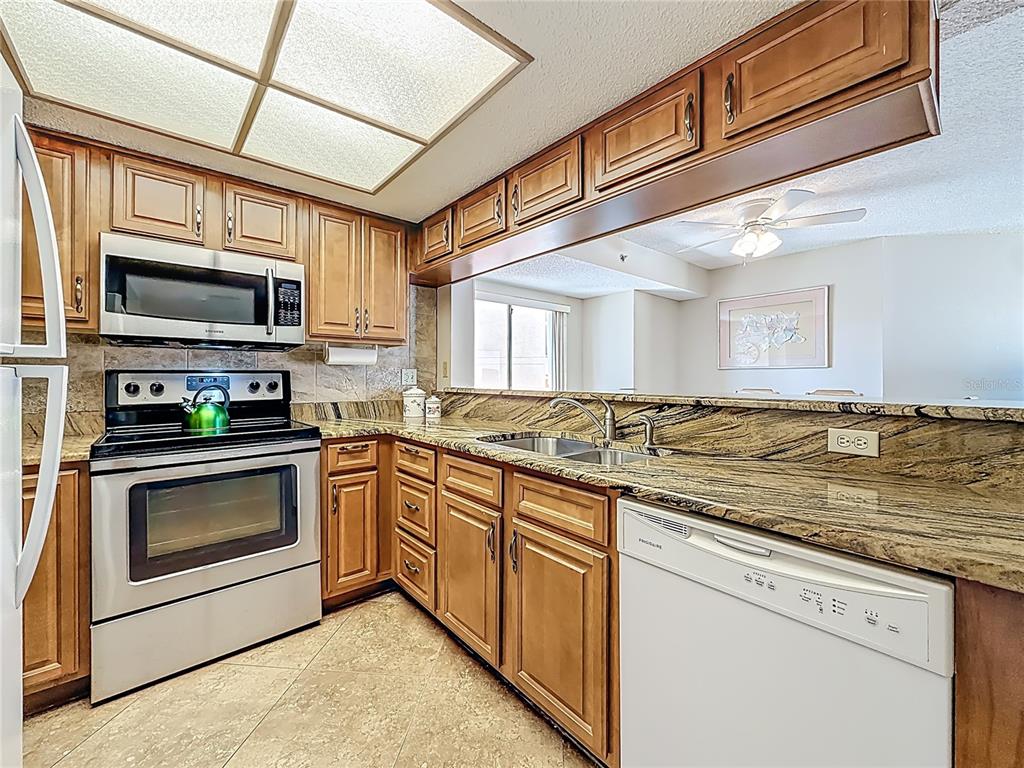 A kitchen features wood cabinets, granite countertops, stainless steel appliances, and a recessed ceiling light — 18450 GULF BOULEVARD UNIT 401, INDIAN SHORES, FL