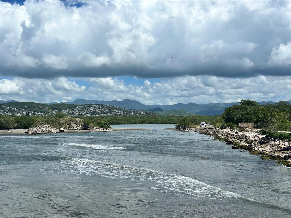 A view of a coastal inlet with rocky shores, mangroves, and distant mountains under a cloudy sky — Lot C ROAD #2, PONCE, PR
