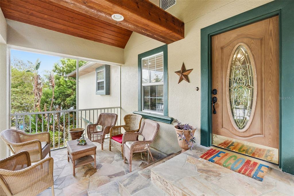 A covered porch features stone flooring, wicker furniture, and a wooden front door with glass — 324 HICKORY COURT, APOPKA, FL