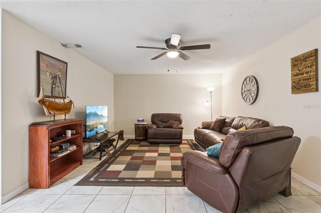 A living room features tile flooring, a ceiling fan, brown leather furniture, and a rug — 324 HICKORY COURT, APOPKA, FL