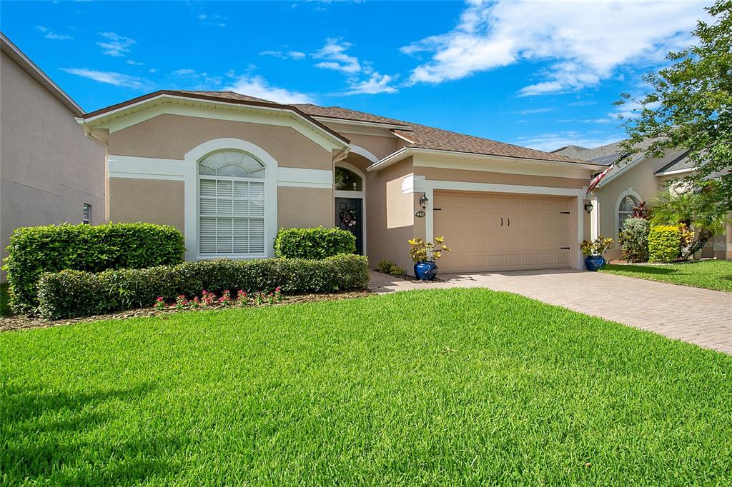 A single-story suburban house with a tan stucco exterior, a two-car garage, and manicured landscaping — 442 HOME GROVE DRIVE, WINTER GARDEN, FL