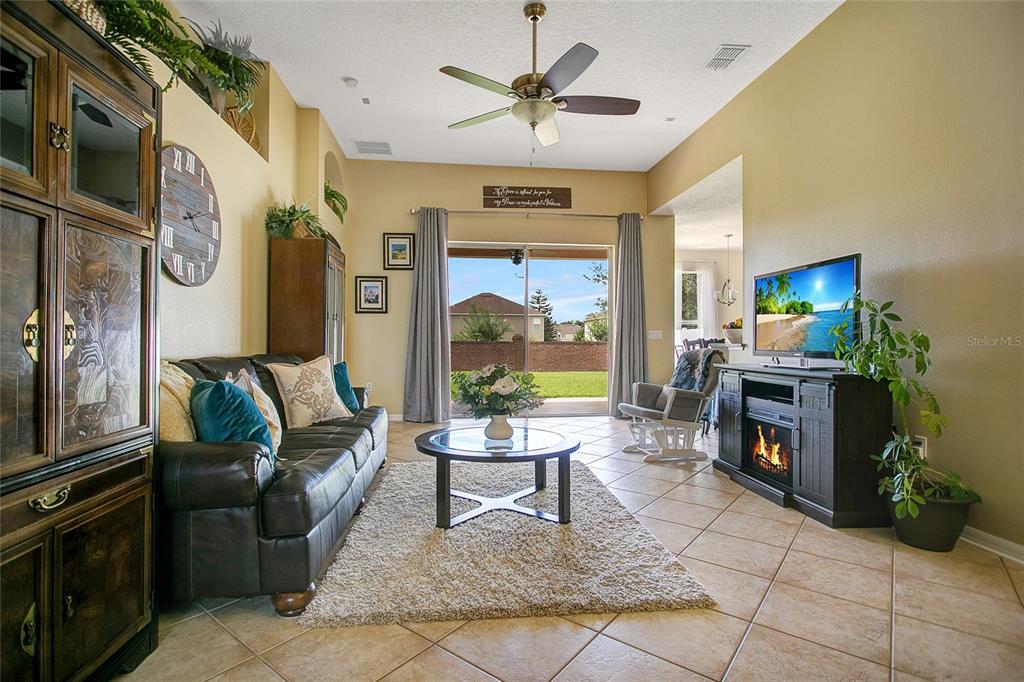 A living room with tile floors, a leather sofa, a fireplace console, and sliding glass doors — 442 HOME GROVE DRIVE, WINTER GARDEN, FL