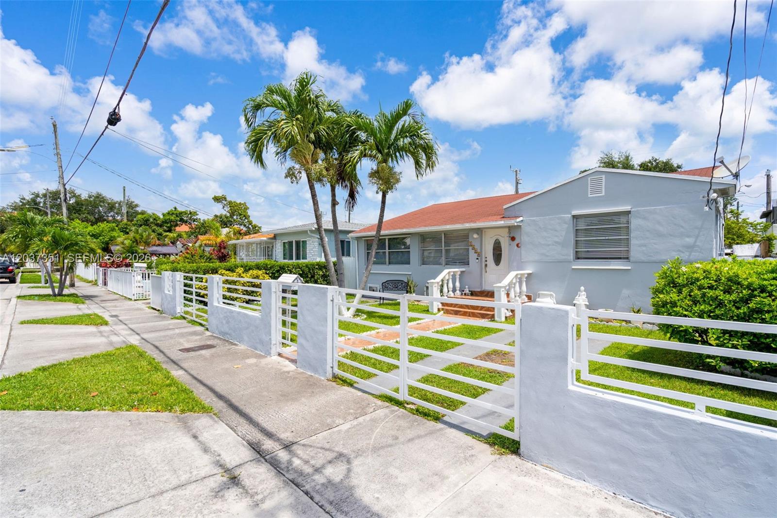 A light blue single-story house features a white fence, palm trees, and a red roof — 2355 SW 1st St, Miami FL 33135, MIAMI, FL