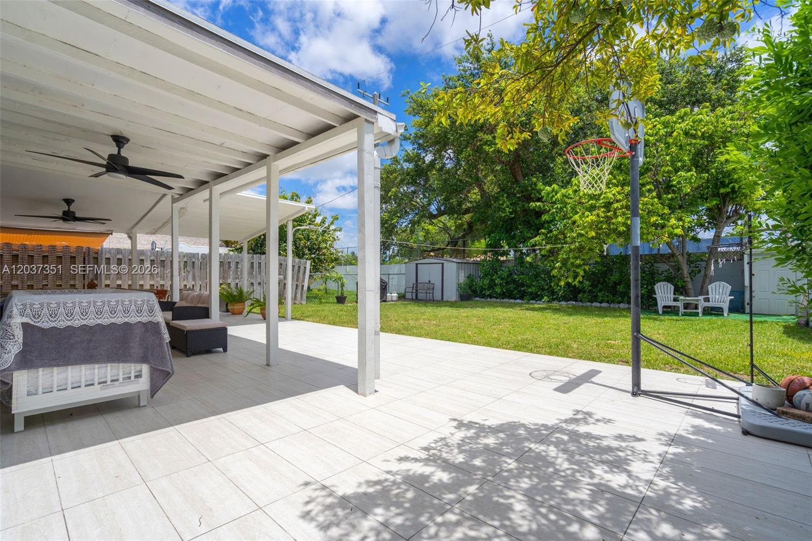 A covered patio with tiled flooring overlooks a grassy backyard featuring a basketball hoop — 2355 SW 1st St, Miami FL 33135, MIAMI, FL