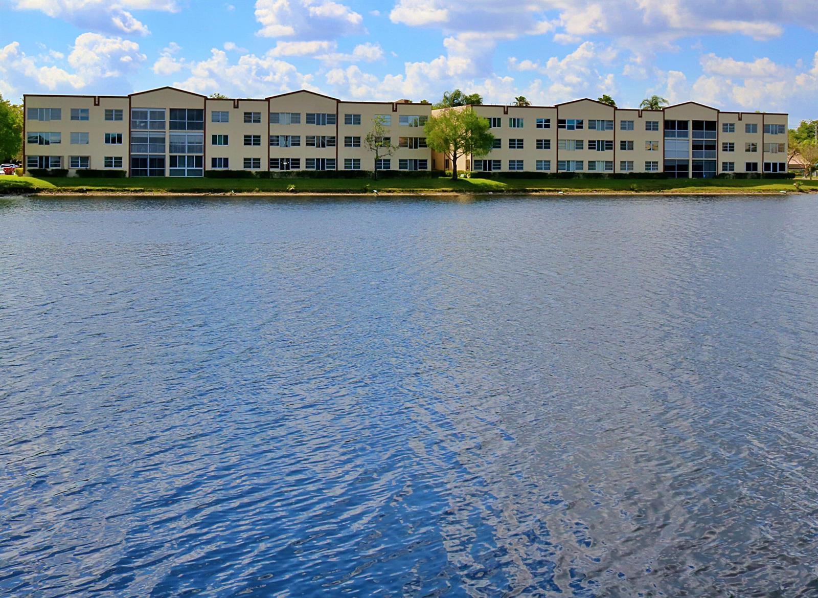 A long, multi-story apartment building sits along the edge of a large, rippling lake — TAMARAC, FL
