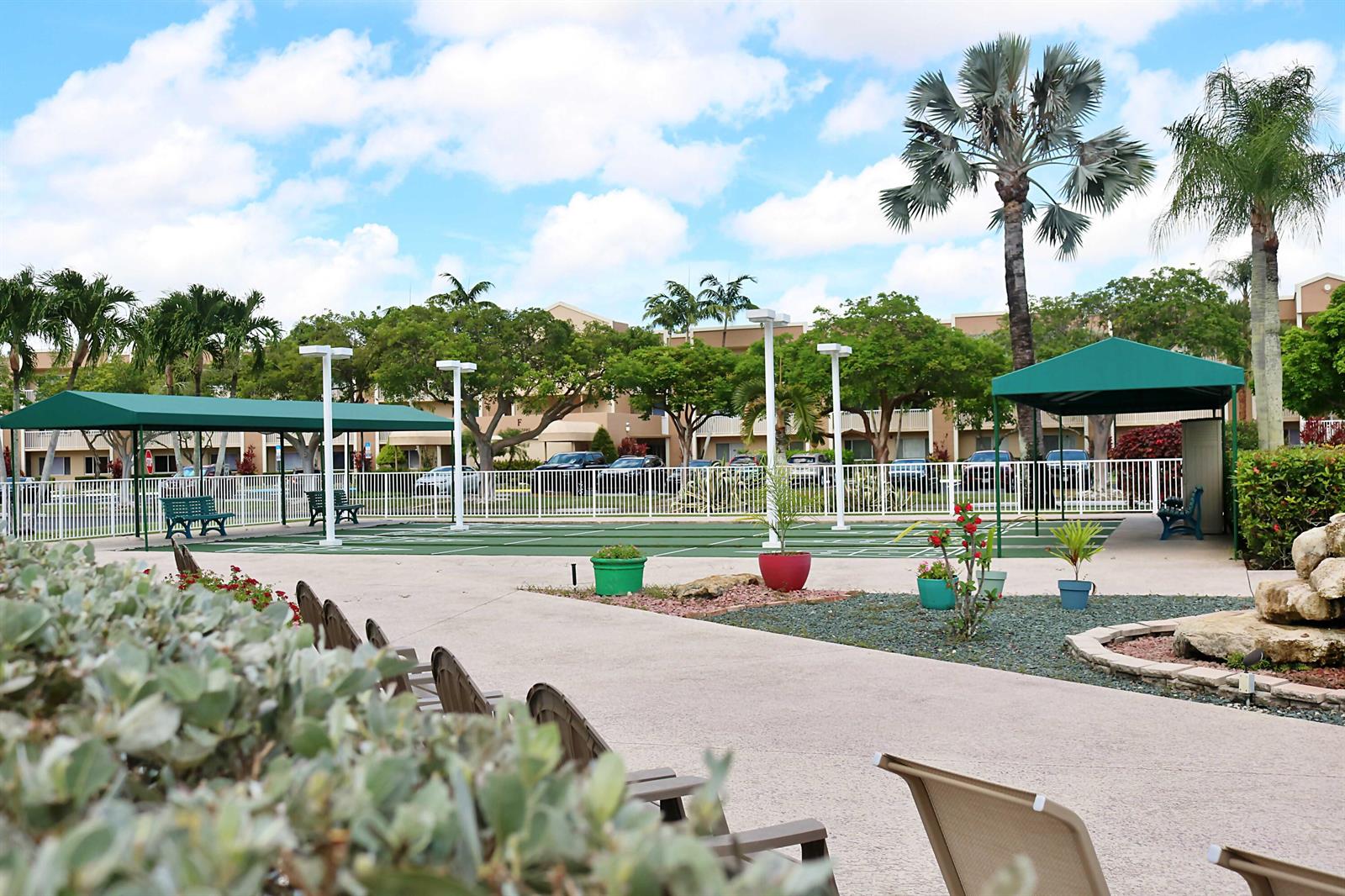 An outdoor shuffleboard court with green awnings and seating sits in front of apartment buildings — TAMARAC, FL