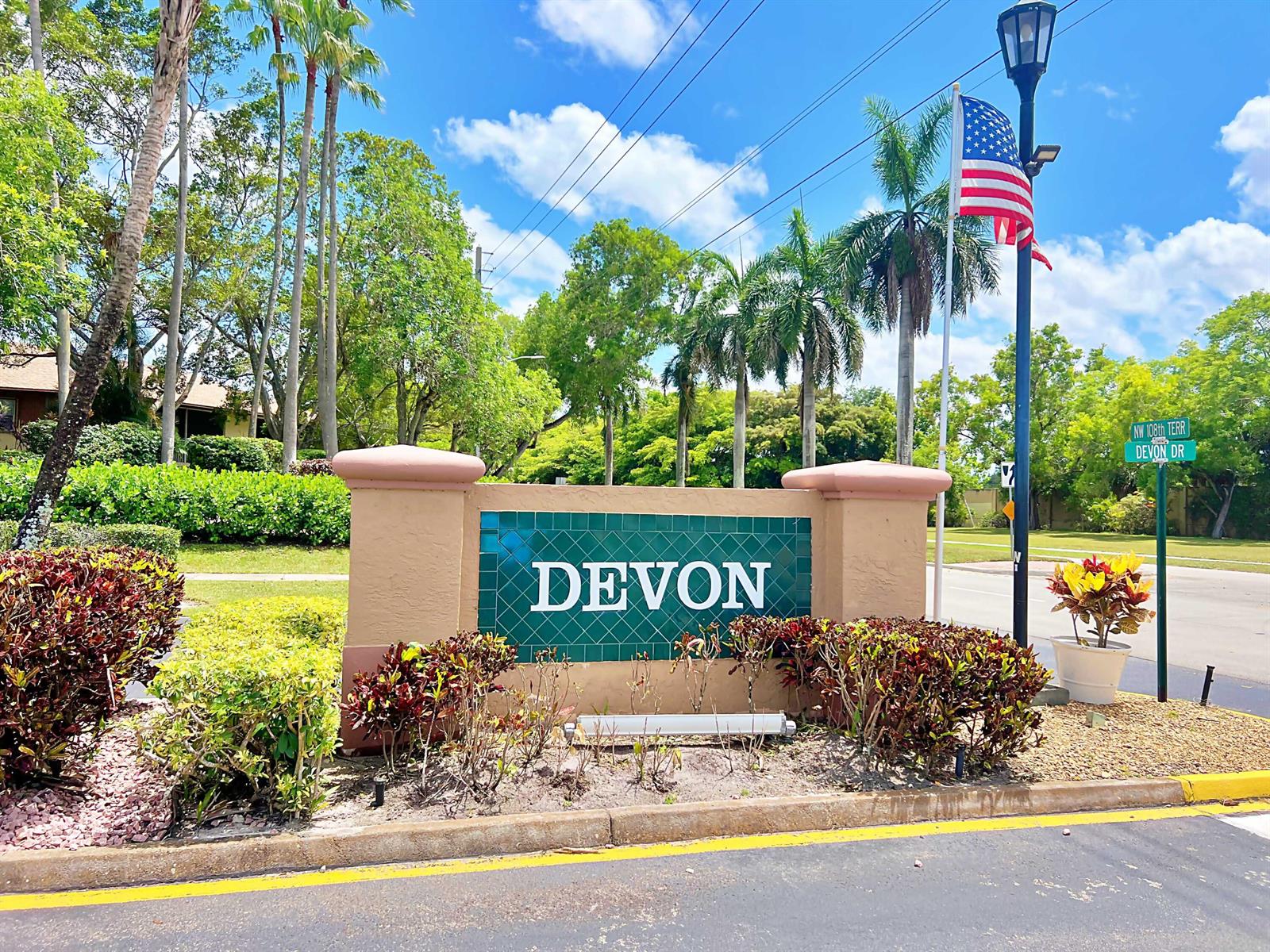 A beige stucco monument sign with green tiles reads "DEVON" near a street corner — TAMARAC, FL