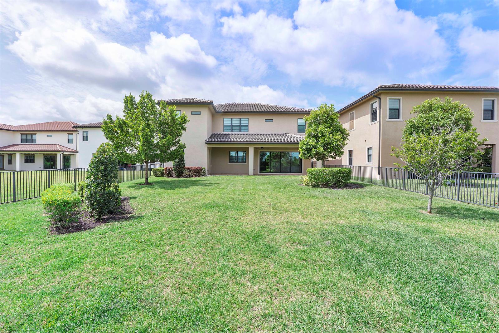 The backyard of a two-story house features a lawn, trees, and a metal fence — 12745 Bayside Court, Parkland FL 33076, PARKLAND, FL