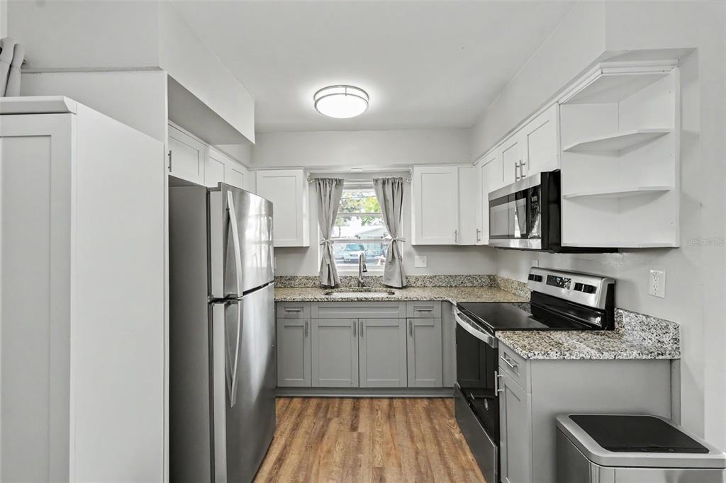 A kitchen features grey lower cabinets, white upper cabinets, stainless steel appliances, and wood flooring — 29 6TH AVENUE SE, LARGO, FL