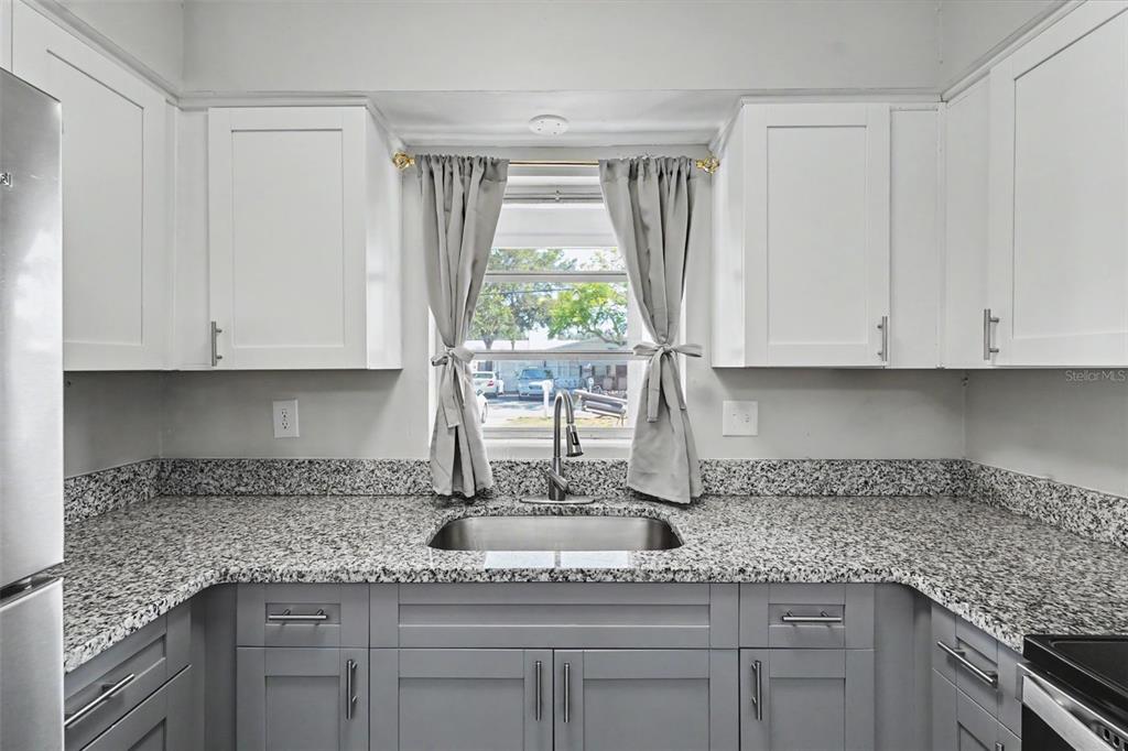 A kitchen features gray lower cabinets, white upper cabinets, granite countertops, and a window sink — 29 6TH AVENUE SE, LARGO, FL