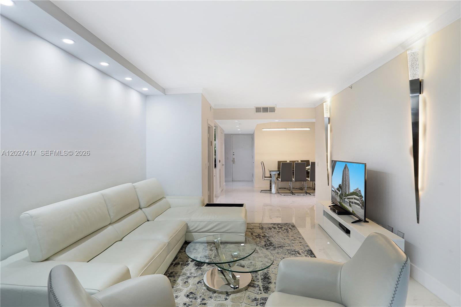 A modern living room features a white sectional sofa, glass coffee table, and television console — 4775 COLLINS AV # 1804, Miami Beach FL 33140, MIAMI BEACH, FL