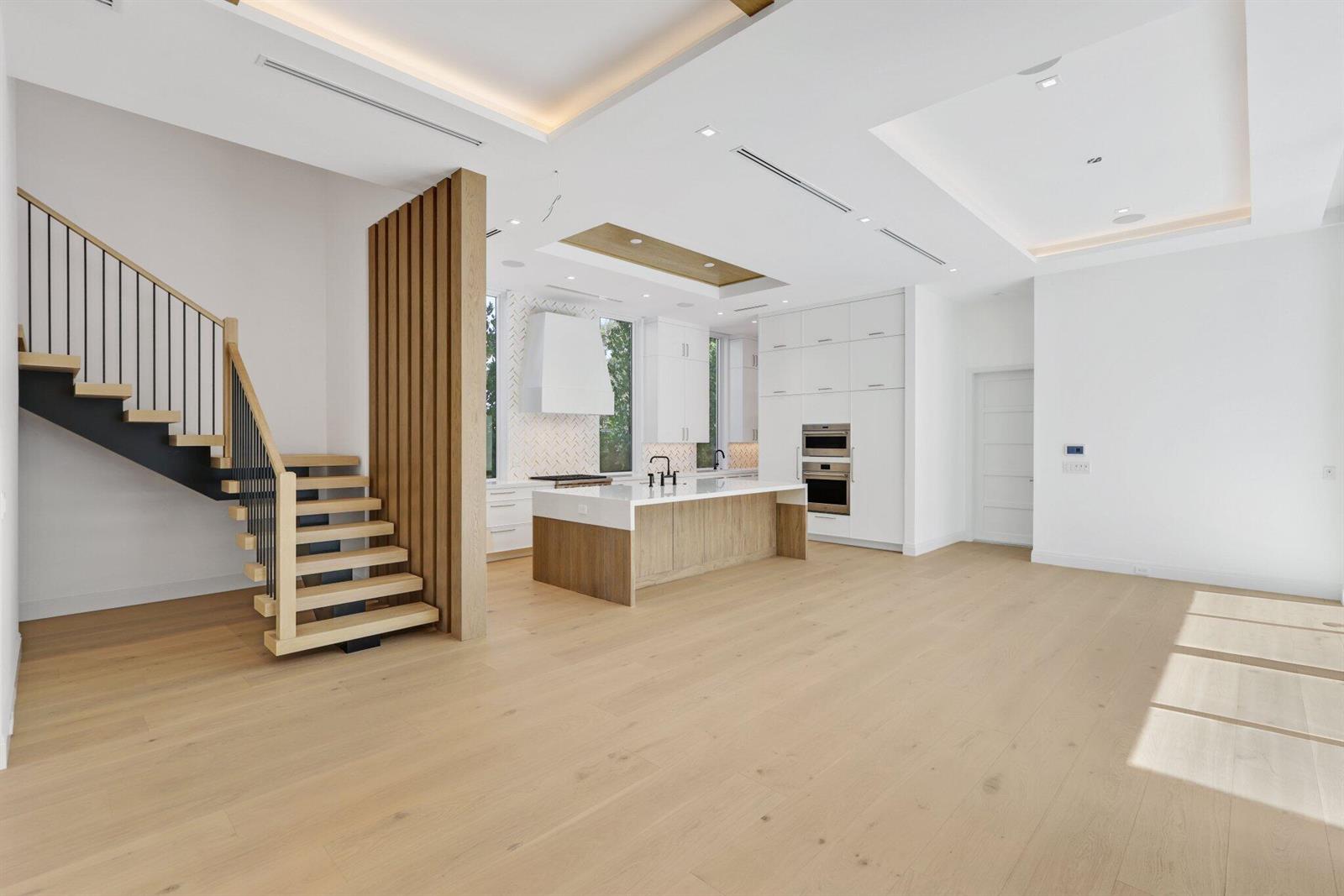 A modern kitchen and living area feature light wood flooring, a central island, and stairs — 330 Grove Place, Delray Beach FL 33444, DELRAY BEACH, FL