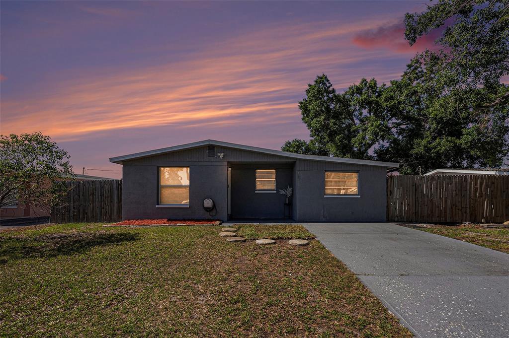A single-story gray house with a driveway and wooden fence under a sunset sky — 4521 W NORTH STREET, TAMPA, FL