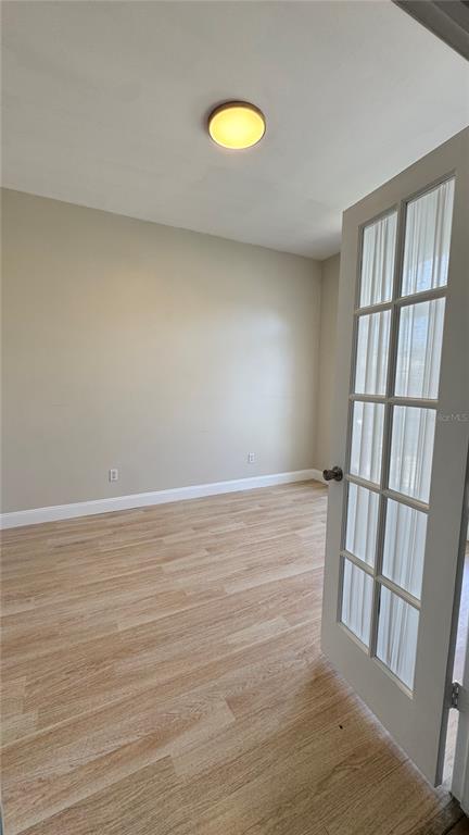 An empty room with light wood-look flooring, beige walls, a ceiling light, and French doors — 1 PRESIDENT LANE, PALM COAST, FL
