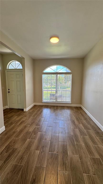 An empty room with wood-look tile flooring, a large arched window, and a front door — 1 PRESIDENT LANE, PALM COAST, FL