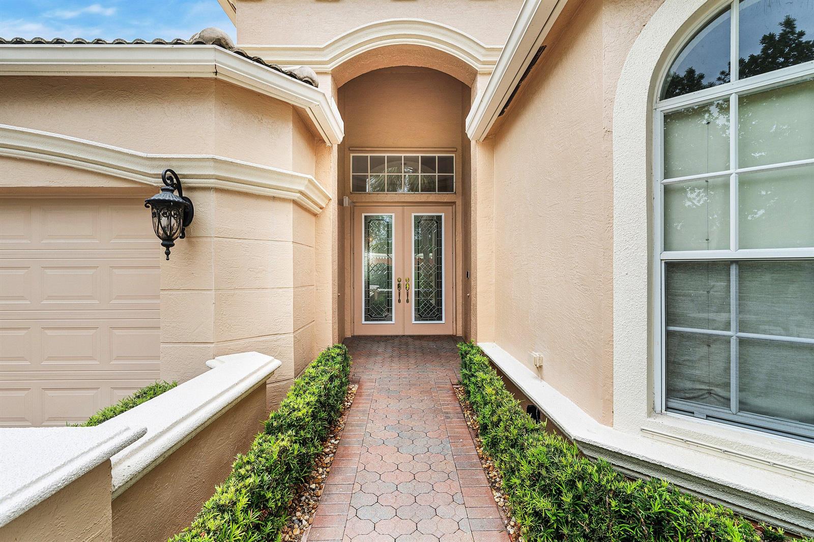 A brick walkway leads to the double front doors of a tan stucco house — 8769 Via Grande E, Wellington FL 33411, WELLINGTON, FL