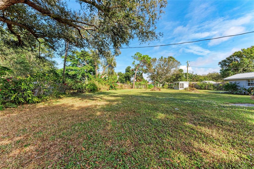 A large, grassy backyard features mature trees, a small shed, and a partial house view — 0 PARK ROAD, VENICE, FL