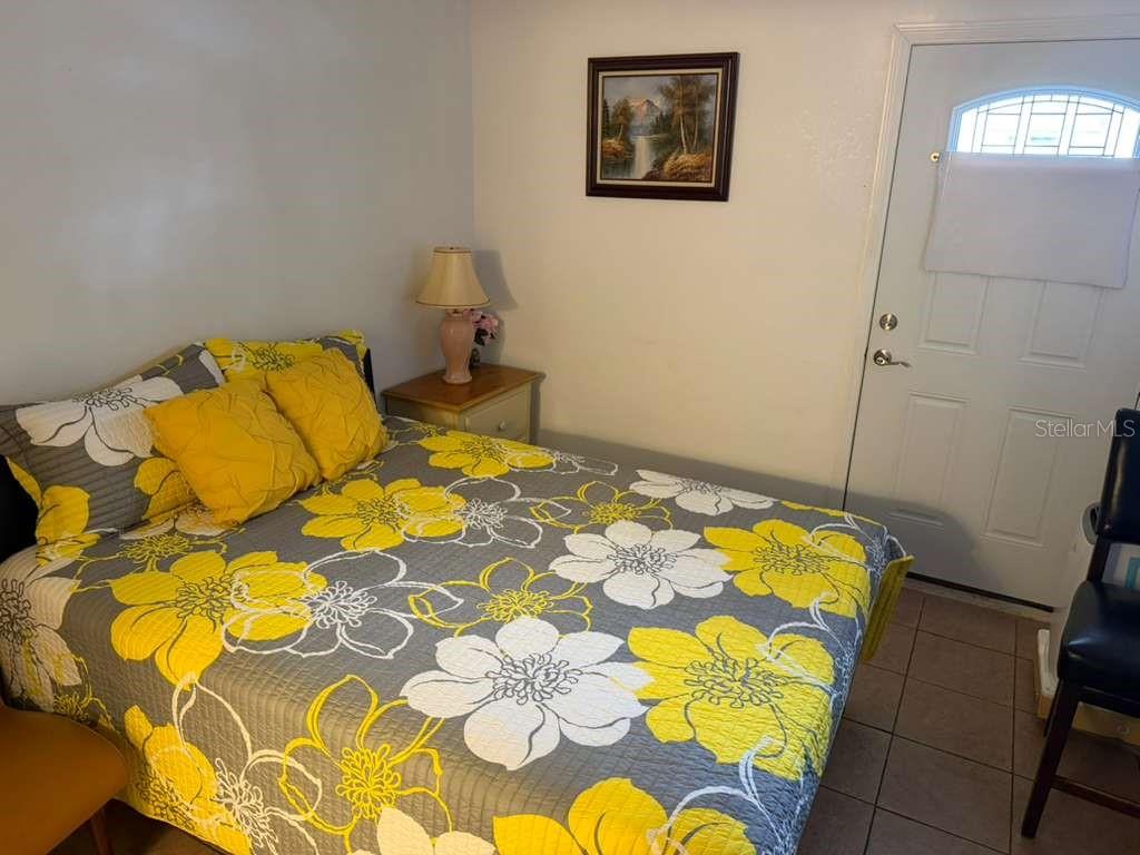 A bedroom features a bed with a yellow and gray floral quilt and a door — 706 BOGIE COURT, KISSIMMEE, FL