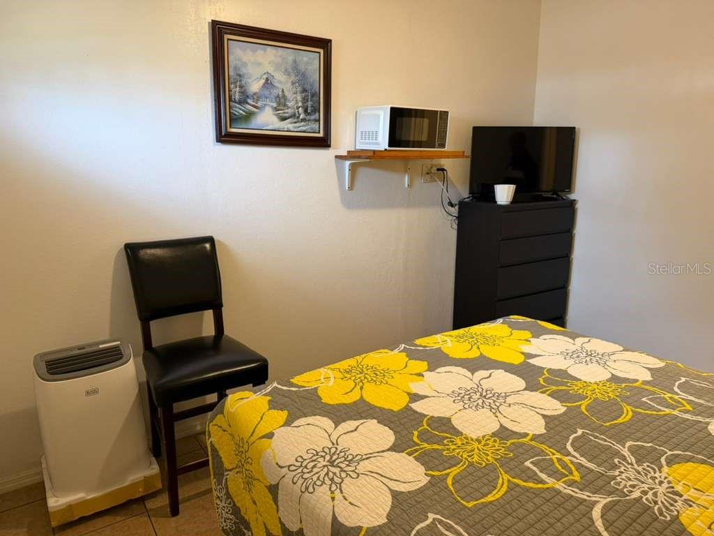 A bedroom features a bed with a floral quilt, a black chair, and a microwave — 706 BOGIE COURT, KISSIMMEE, FL