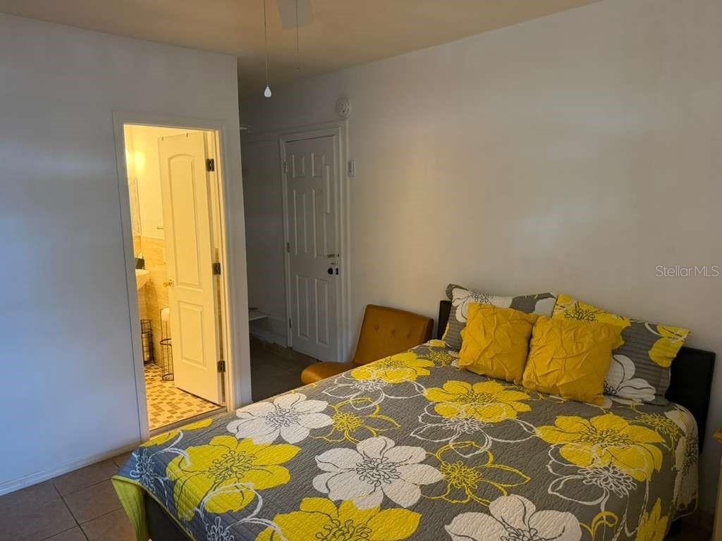 A bedroom features a bed with a yellow and gray floral quilt and an attached bathroom — 706 BOGIE COURT, KISSIMMEE, FL
