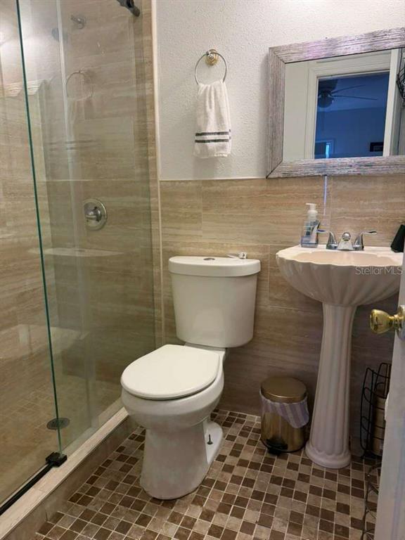 A bathroom features a glass-enclosed shower, a white toilet, and a pedestal sink — 706 BOGIE COURT, KISSIMMEE, FL