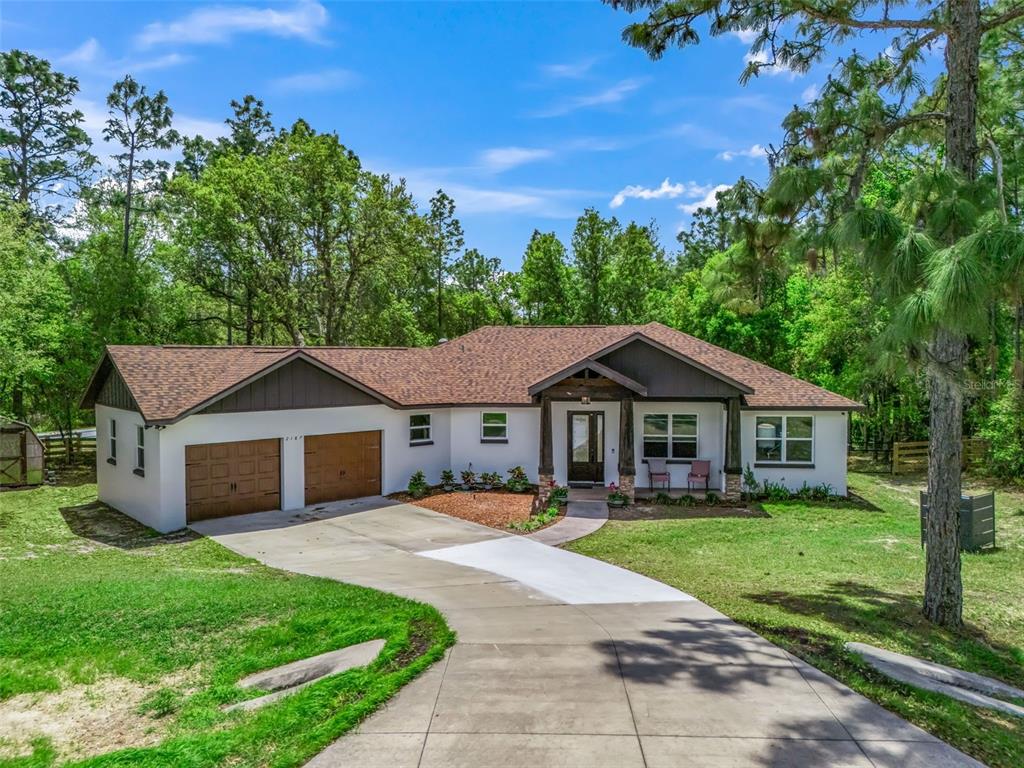 A single-story house with a white exterior, brown garage doors, and a shingled roof — 2187 COUNTY ROAD 243C, WILDWOOD, FL