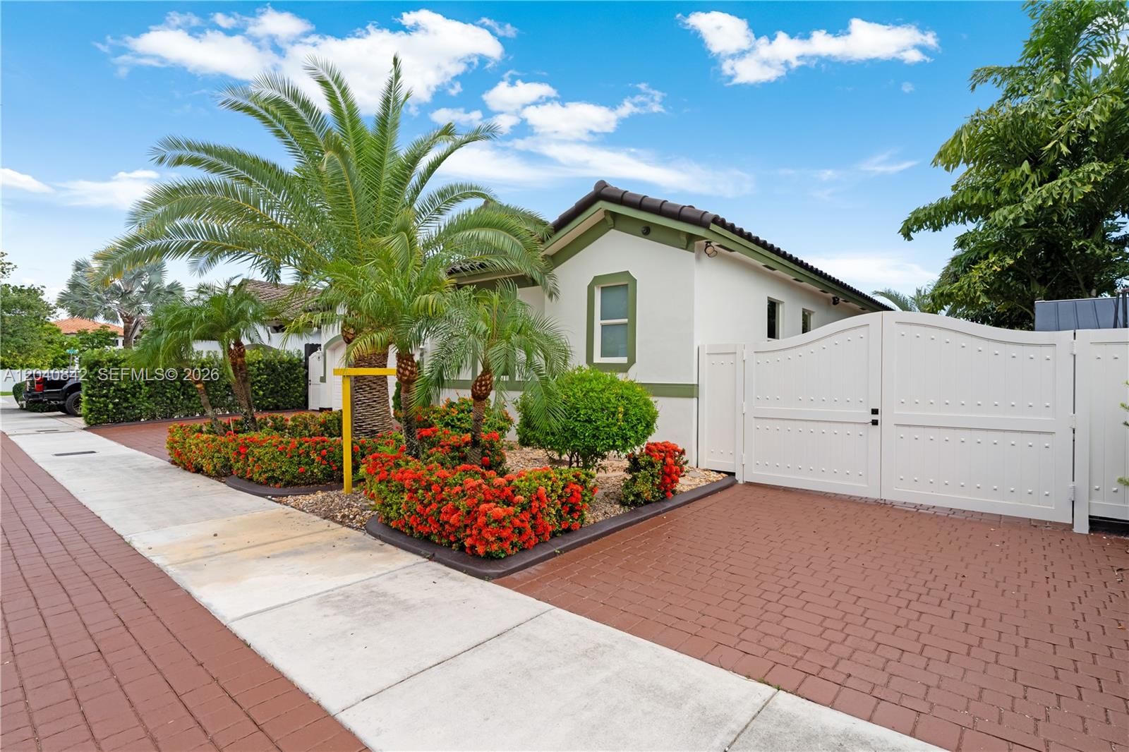 A white house with a gated driveway and a landscaped garden featuring palm trees — 2351 SW 145th Ave, Miami FL 33175, MIAMI, FL