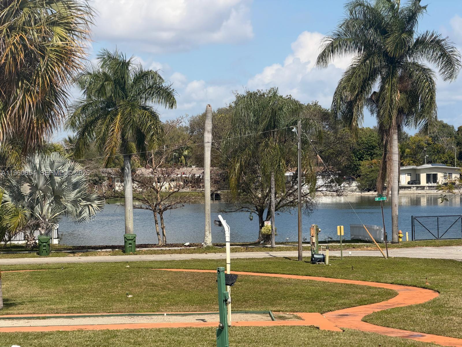 A view of a lake from a grassy yard with palm trees and a walkway — 725 SW 11th Ave # 17F, Hallandale Beach FL 33009, HALLANDALE BEACH, FL