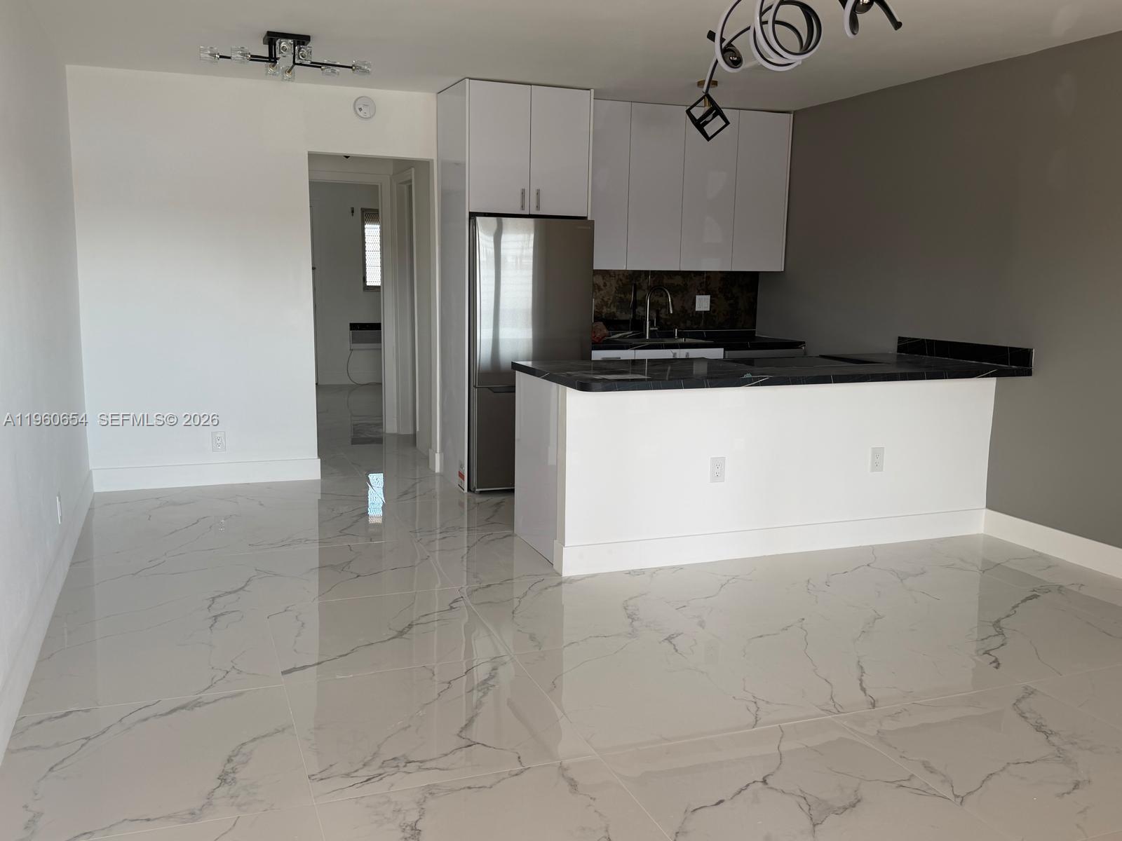 A modern kitchen features white cabinets, a stainless steel refrigerator, and a black countertop island — 725 SW 11th Ave # 17F, Hallandale Beach FL 33009, HALLANDALE BEACH, FL
