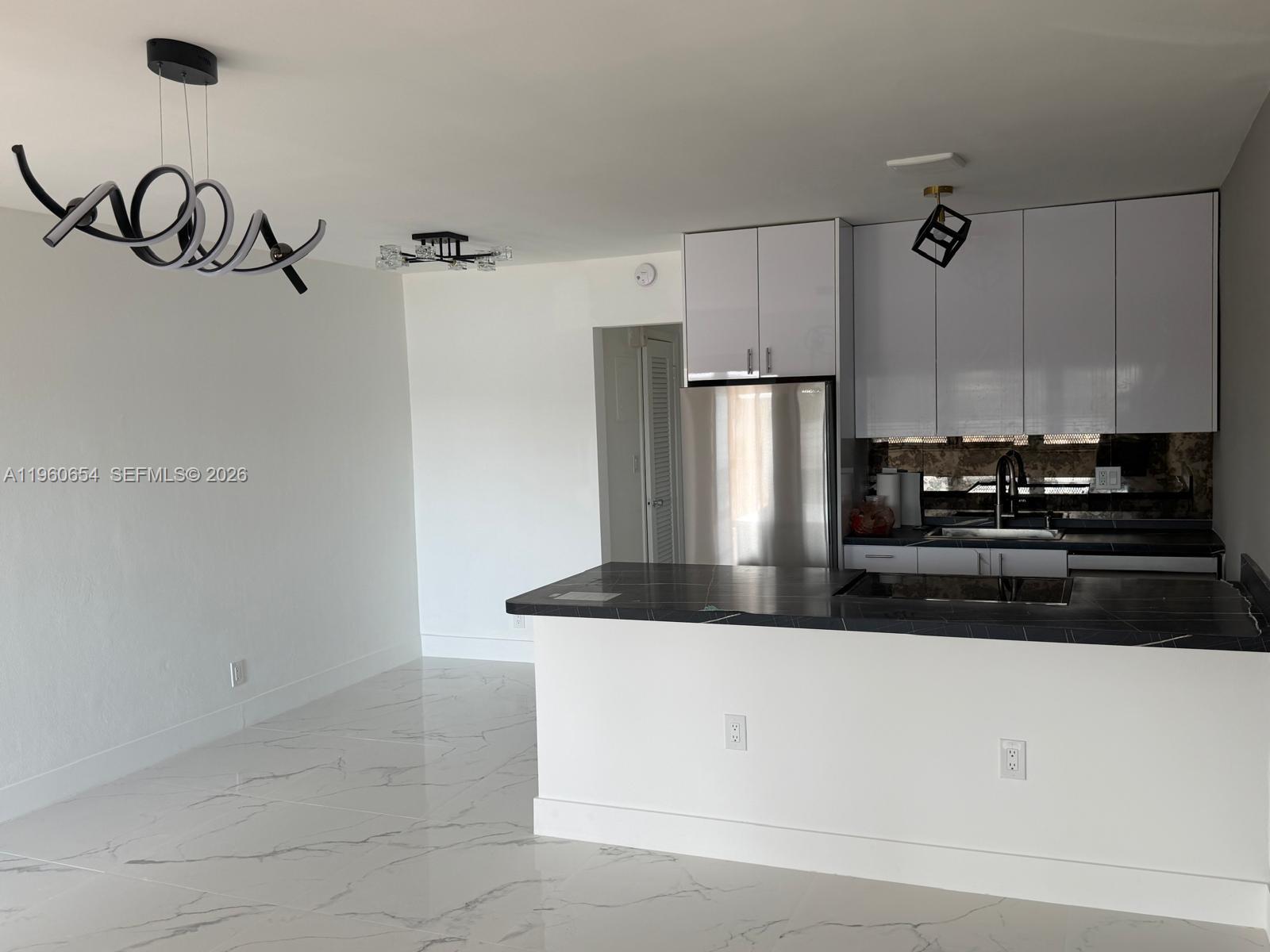 A modern kitchen features white cabinets, dark marble countertops, and white marble-patterned tile flooring — 725 SW 11th Ave # 17F, Hallandale Beach FL 33009, HALLANDALE BEACH, FL