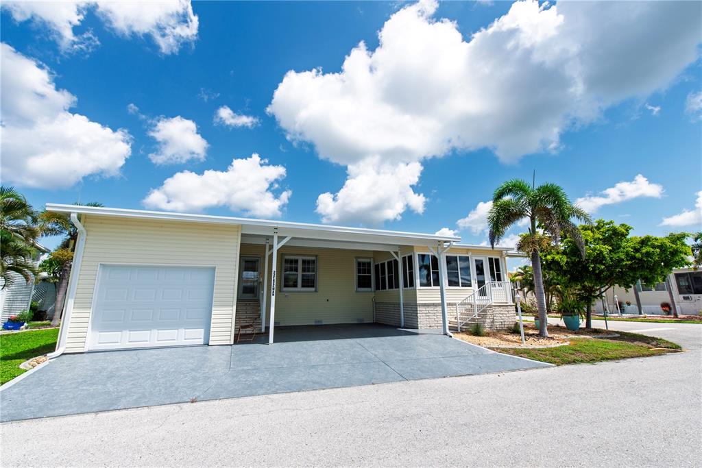 A light yellow manufactured home features a white garage door, a carport, and a palm tree — 22 FREEMAN AVENUE, PUNTA GORDA, FL