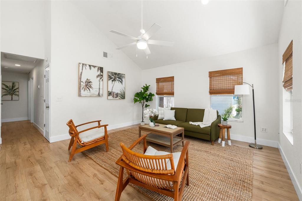 A bright living room features a green sofa, two wooden chairs, and a jute rug — 3177 NW 9TH TERRACE, GAINESVILLE, FL