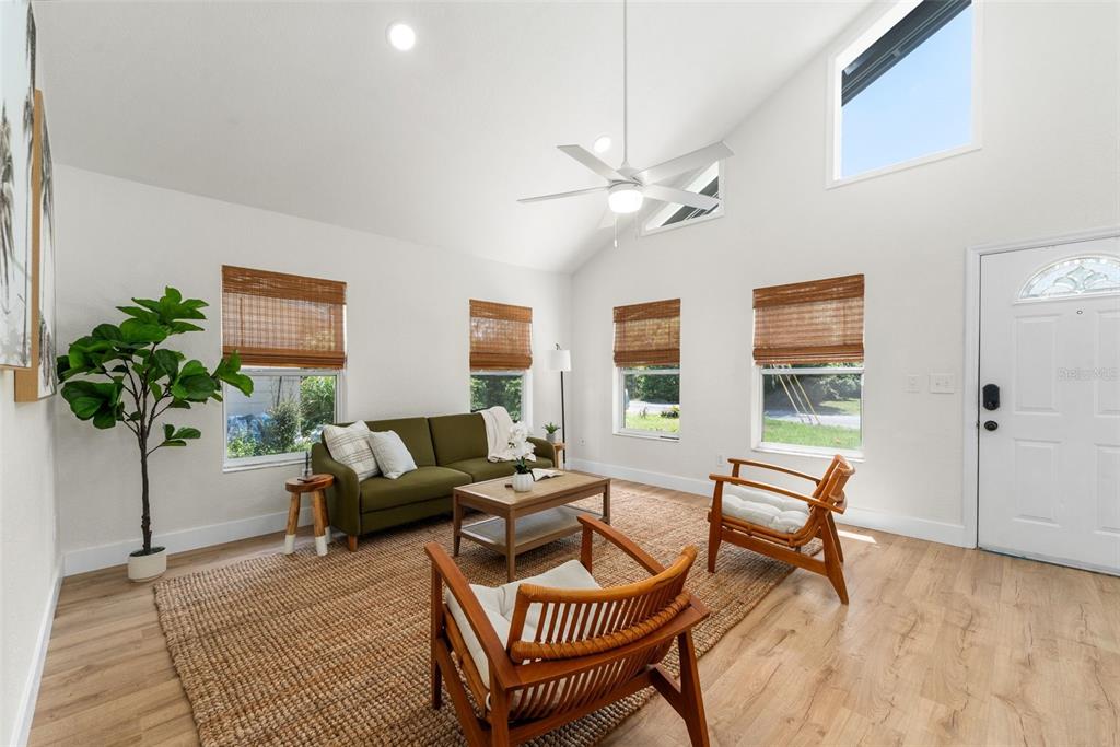 A bright living room features a vaulted ceiling, wood-look flooring, and a green sofa — 3177 NW 9TH TERRACE, GAINESVILLE, FL