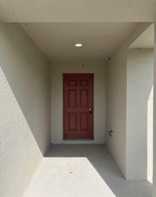 A red front door is centered at the end of a covered concrete entryway — 5480 SILTSTONE STREET, LAKELAND, FL