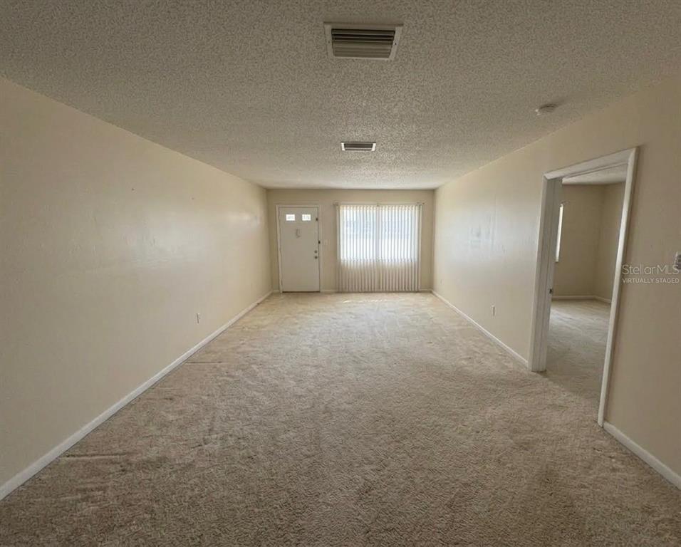An empty living room features beige carpeting, light-colored walls, a front door, and vertical blinds — 5860 38TH AVENUE N UNIT 29, ST PETERSBURG, FL