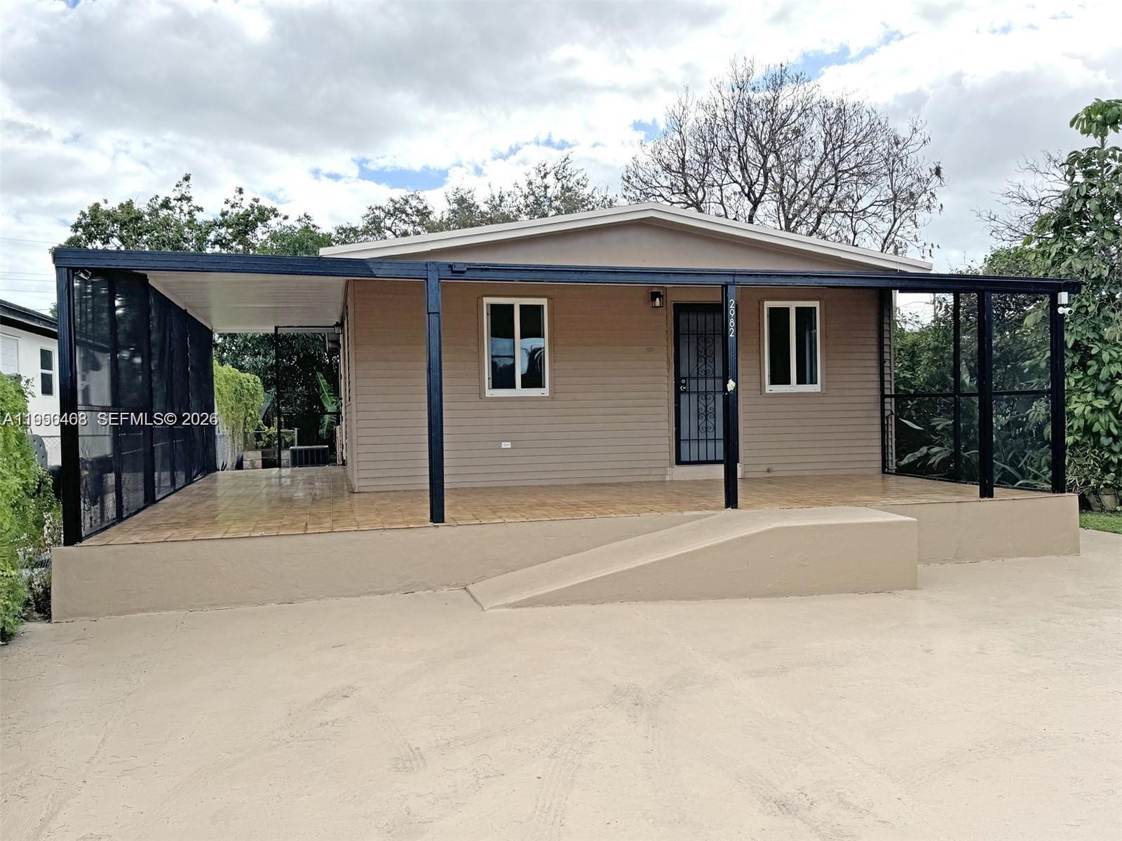 A tan house features a large covered front porch with a ramp and black screening — 2982 NW 95th St, Miami FL 33147, MIAMI, FL