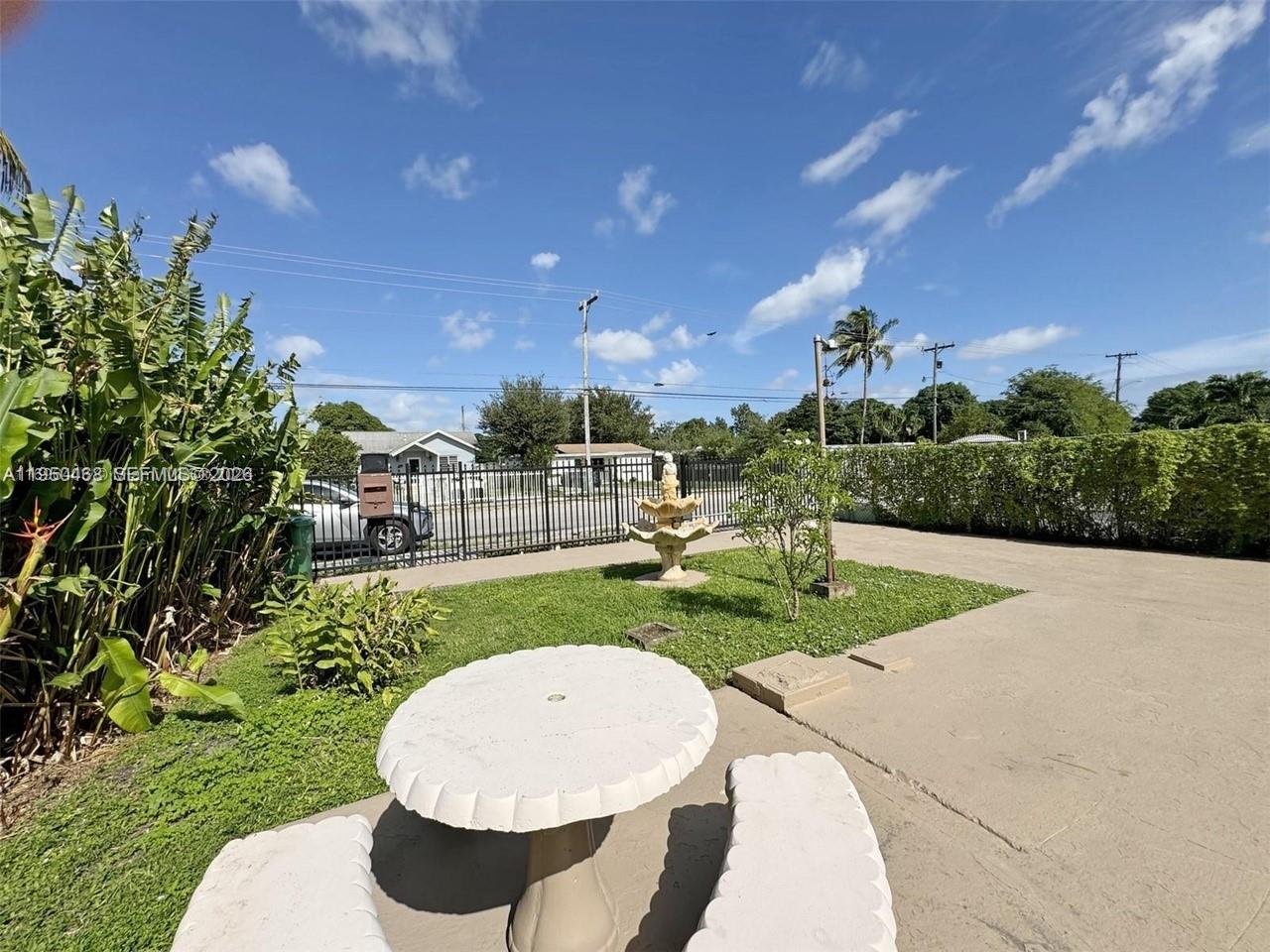 A concrete patio features a stone table, a small fountain, and a black metal fence — 2982 NW 95th St, Miami FL 33147, MIAMI, FL