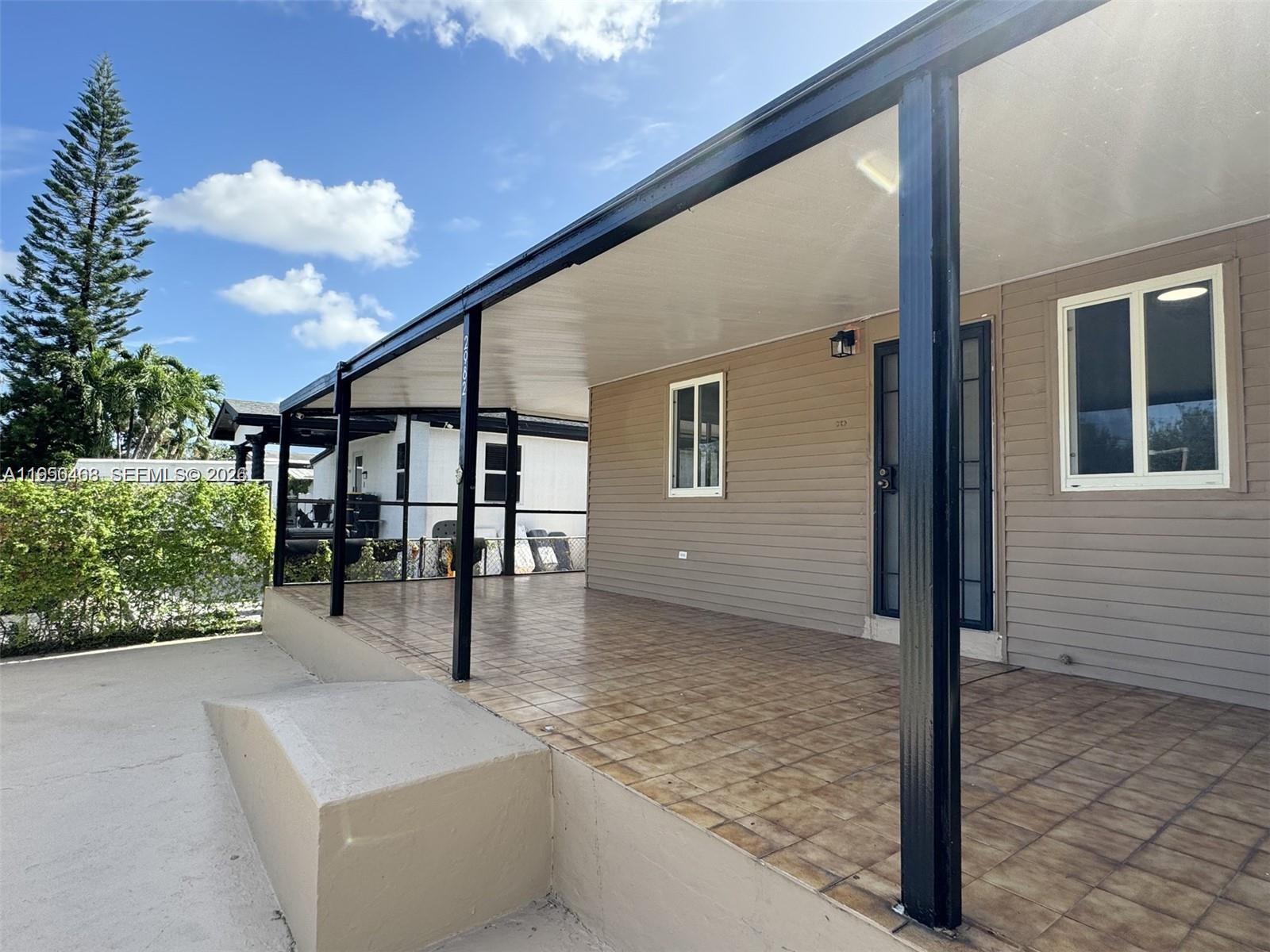 A covered tiled porch features black support columns and tan siding on a house exterior — 2982 NW 95th St, Miami FL 33147, MIAMI, FL