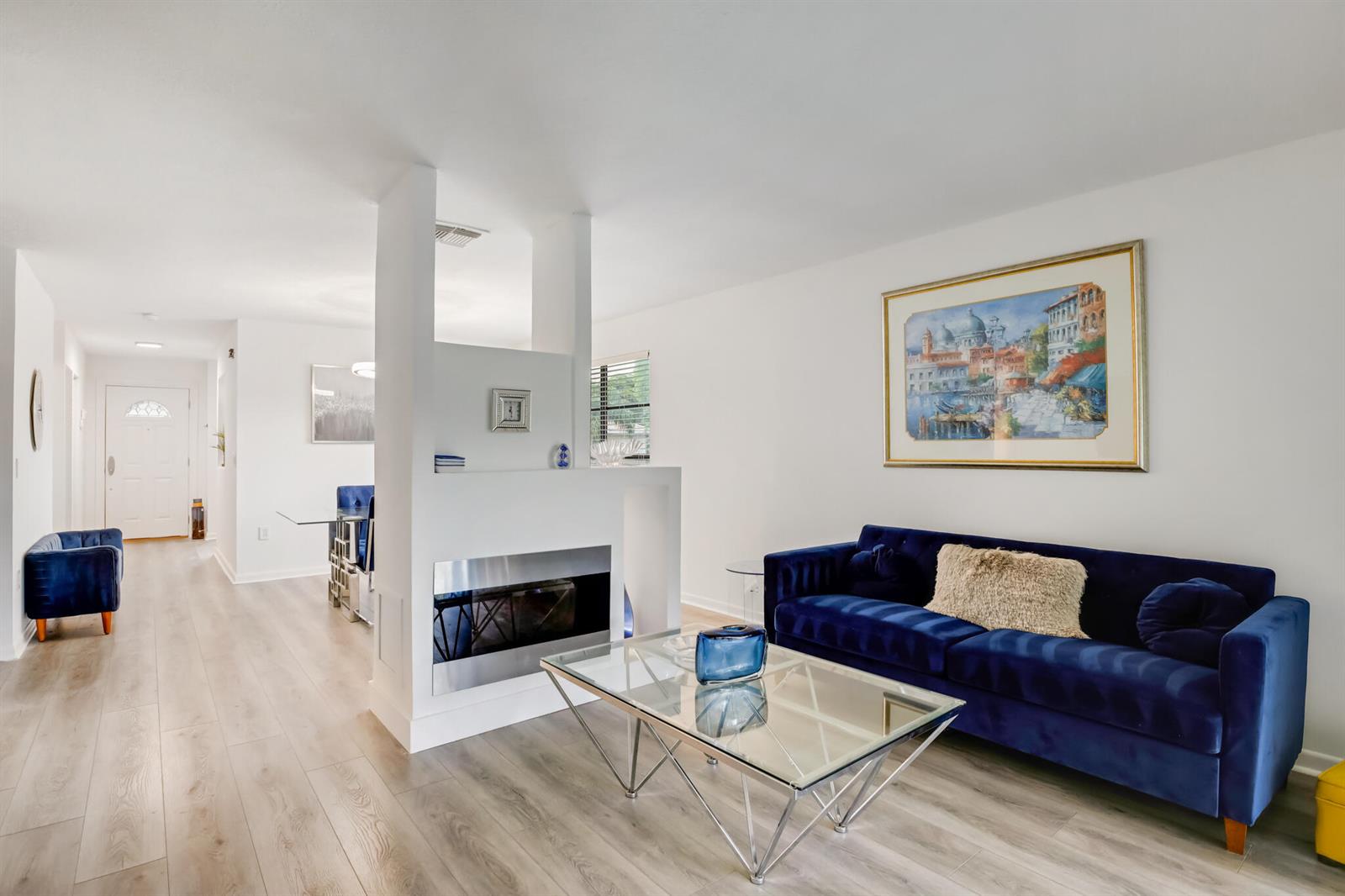 A living room with a blue velvet sofa, glass coffee table, and a central fireplace — BOYNTON BEACH, FL