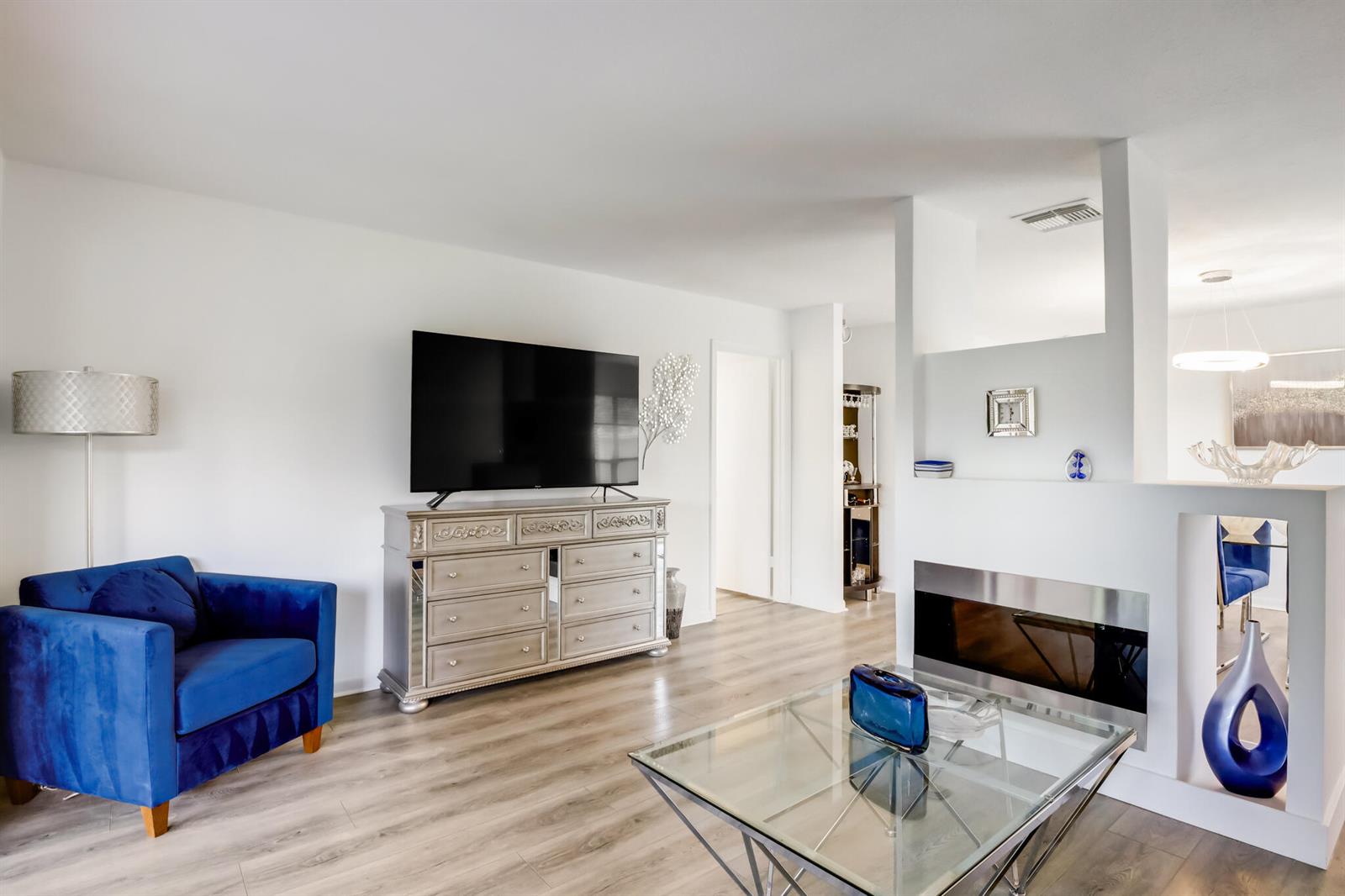 A living room features a blue armchair, a mirrored dresser, a fireplace, and glass table — BOYNTON BEACH, FL