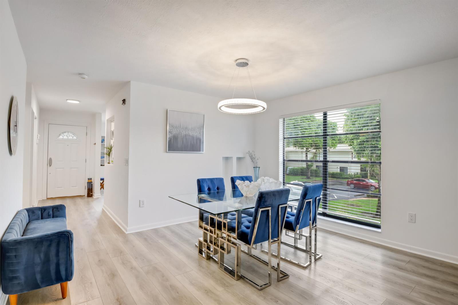 A dining room features a glass table, blue velvet chairs, and a modern circular light fixture — BOYNTON BEACH, FL
