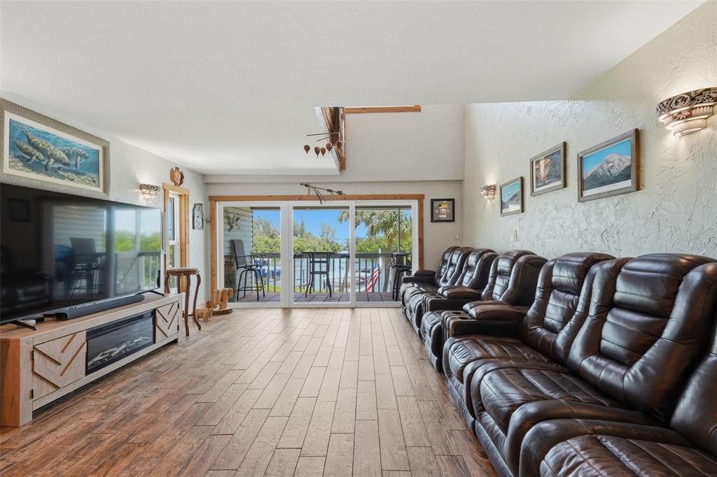 A living room features wood-look tile floors, a large television, and a row of recliners — 1375 PINELLAS BAYWAY S UNIT 39, TIERRA VERDE, FL